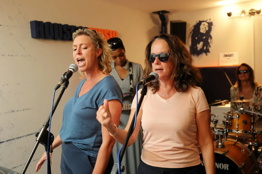 Twee zangeressen zingen samen achter de microfoon terwijl de band achter hen repeteert
